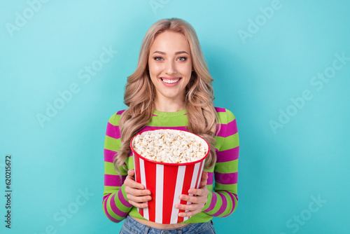 Photo of optimistic satisfied woman with curly hairstyle dressed striped sweatshirt hold popcorn basket isolated on teal color background