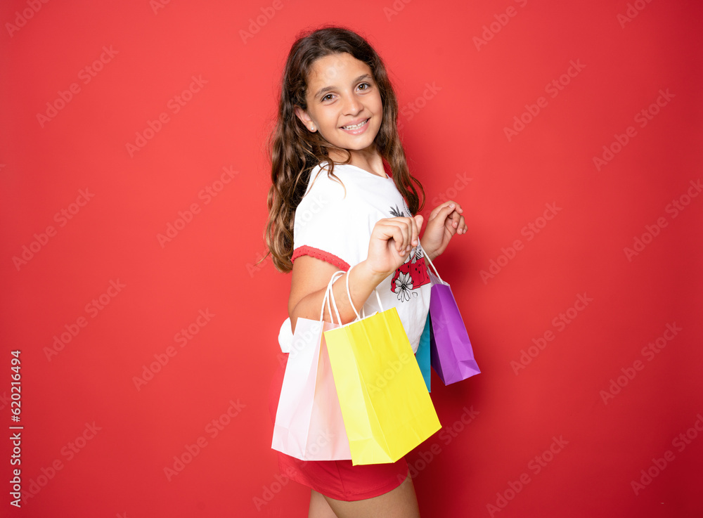 Beautiful brunette little girl holding shopping bags isolated over red background.