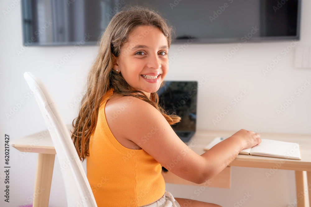 Head shot close up portrait of happy small pupil learning at home. Smiling little child girl enjoying doing lessons in living room. Smart kid schoolgirl looking at camera, studying remotely online. Head shot close up portrait of happy small pupil learning at home. Smiling little child girl enjoying doing lessons in living room. Smart kid schoolgirl looking at camera, studying remotely online.