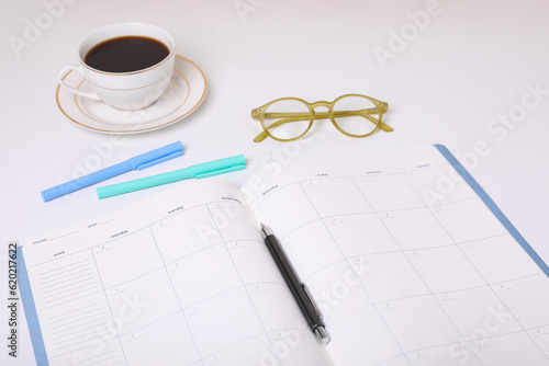Open monthly planner, coffee, glasses and stationery on white background