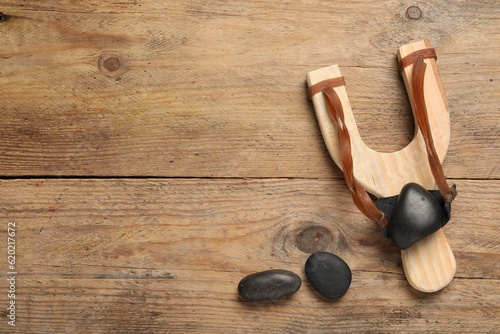 Slingshot with stones on wooden background, flat lay. Space for text