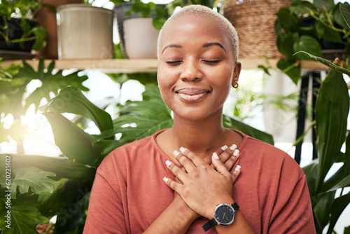 Zen, breathing and calm woman by plants for breathing exercise in meditation in a nursery. Breathe, gratitude and young African female person with a relaxing mindset by an indoor greenhouse garden.