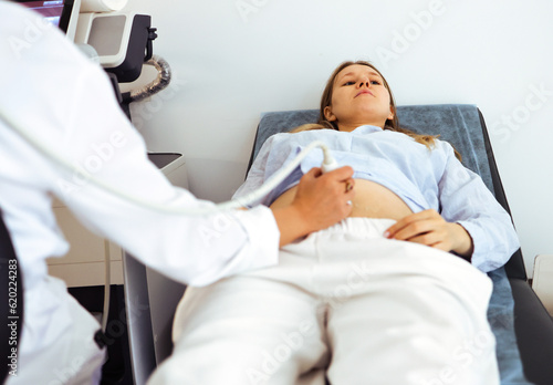 the doctor's hand holds an ultrasound scanner on the stomach of a pregnant woman lying on a couch. pregnancy screening in the clinic. middle plan