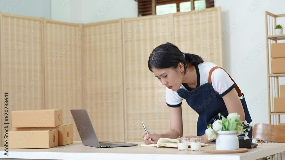 A portrait of a small start-up and SME owner, an Asian female entrepreneur using notebooks and laptop, checking orders to organize products before packing them into inner boxes for customers. A portrait of a small start-up and SME owner, an Asian female entrepreneur using notebooks and laptop, checking orders to organize products before packing them into inner boxes for customers.