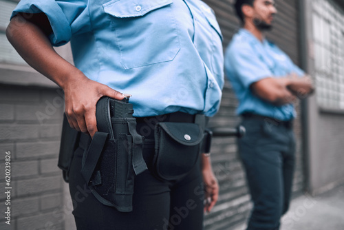 Hand, gun and security with a police officer on duty or patrol in the city for safety and law enforcement. Legal, service and armed response with a guard outdoor in an urban town for crime prevention