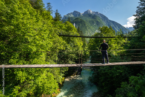 Adventure hiker walking on suspension bridge over river in mountains