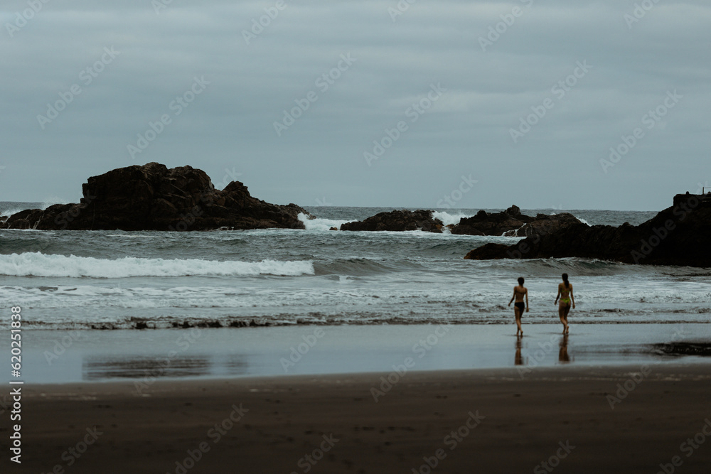 two girls walking to the wild water on dark beach