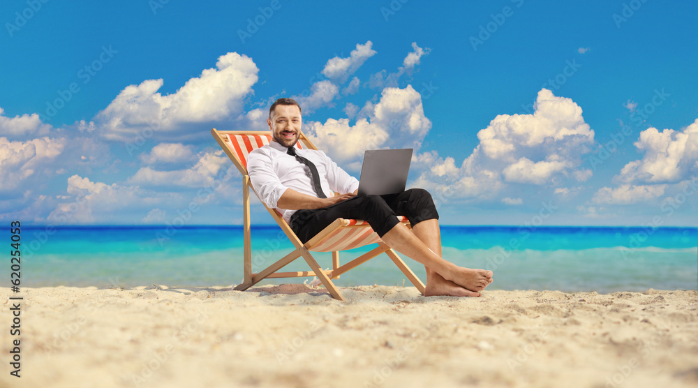 Businessman sitting on a deck chair and using a laptop computer on a beach