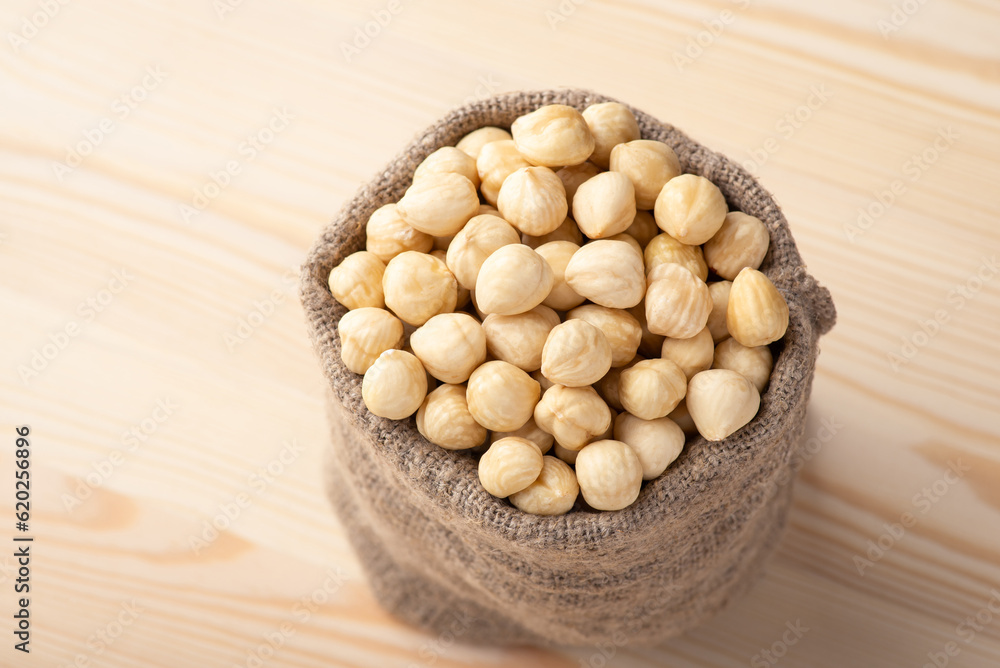 Small linen bag with hazelnuts on wooden background. Tasty peeled hazelnuts