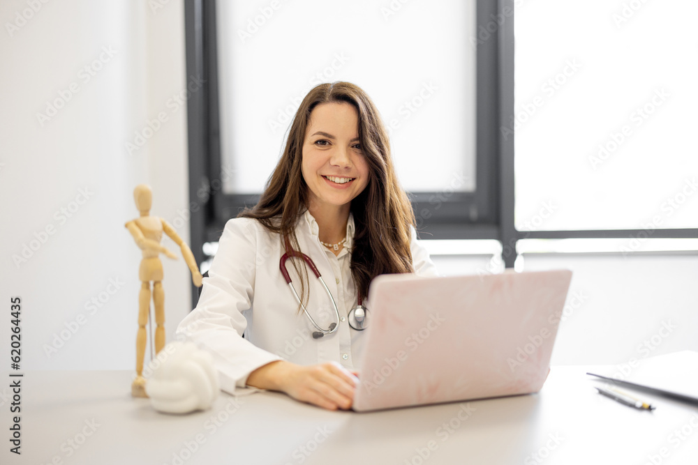 Portrait of a cheerful female doctor sitting with laptop in medical office. Medical director of a private clinic Portrait of a cheerful female doctor sitting with laptop in medical office. Medical director of a private clinic