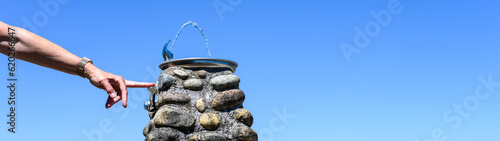 Hand holding down lever on water fountain, refreshing on a sunny summer day outside in fresh air, classic river rock and mortar pillar as base for fountain
 photo