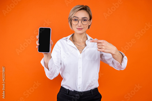 Optimistic woman wearing white official style shirt pointing at empty display of mobile phone