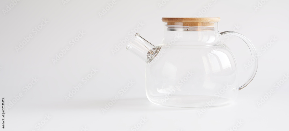 A transparent teapot made of tempered glass with a wooden lid and a metal spiral strainer on a white background. Element of modern trendy kitchen interior A transparent teapot made of tempered glass with a wooden lid and a metal spiral strainer on a white background. Element of modern trendy kitchen interior