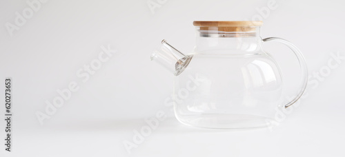 A transparent teapot made of tempered glass with a wooden lid and a metal spiral strainer on a white background. Element of modern trendy kitchen interior