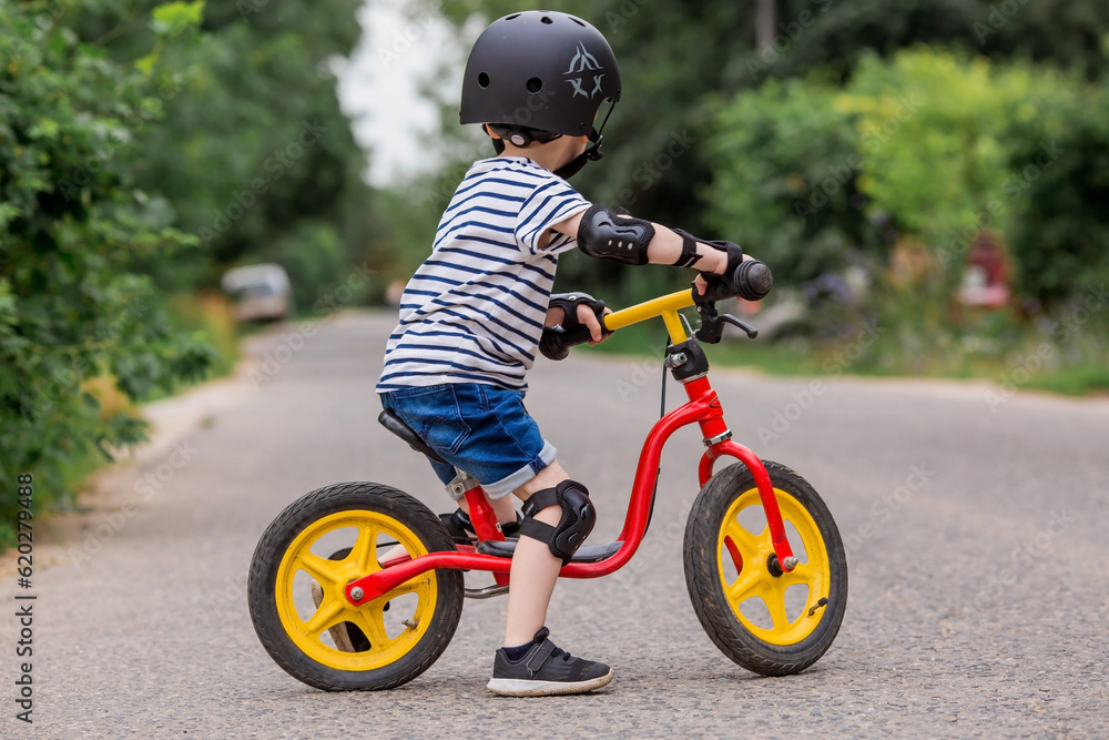 A cheerful little boy rides a running bike in a helmet outdoors. A happy child is engaged in an active sport. Protection. Life insurance and child safety. A cheerful little boy rides a running bike in a helmet outdoors. A happy child is engaged in an active sport. Protection. Life insurance and child safety.