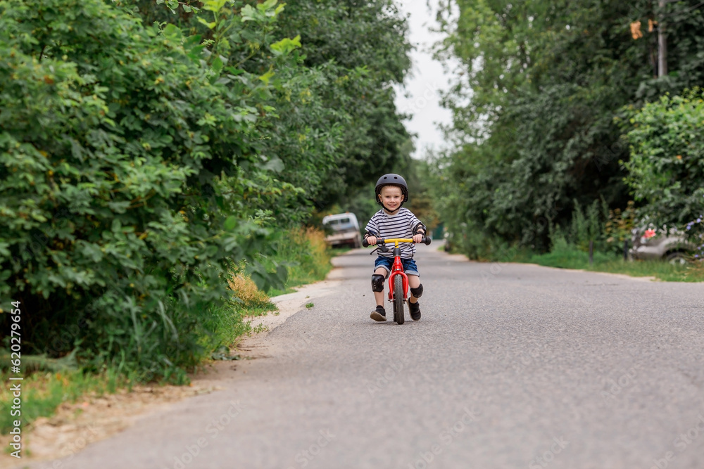 A cheerful little boy rides a running bike in a helmet outdoors. A happy child is engaged in an active sport. Protection. Life insurance and child safety. A cheerful little boy rides a running bike in a helmet outdoors. A happy child is engaged in an active sport. Protection. Life insurance and child safety.