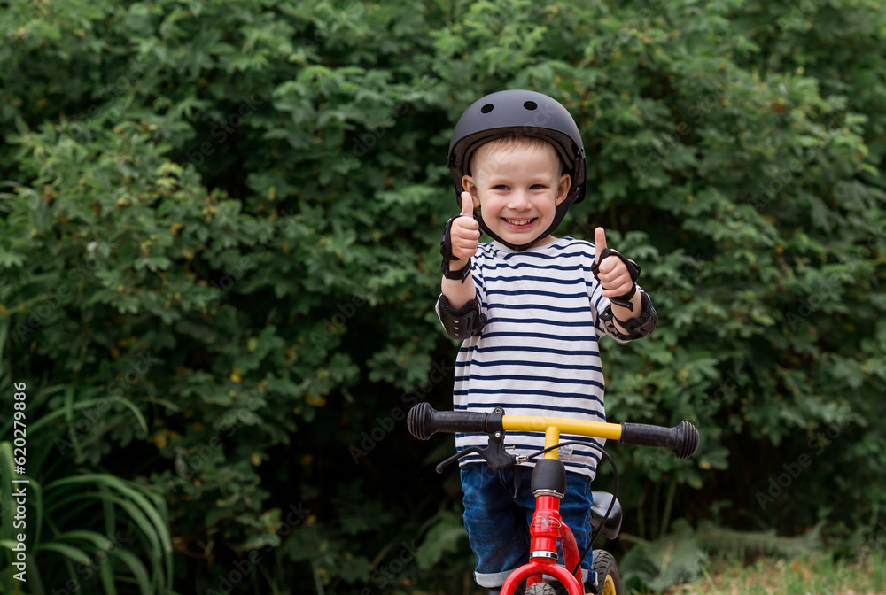 A cheerful little boy rides a running bike in a helmet outdoors. A happy child is engaged in an active sport. Protection. Life insurance and child safety. A cheerful little boy rides a running bike in a helmet outdoors. A happy child is engaged in an active sport. Protection. Life insurance and child safety.