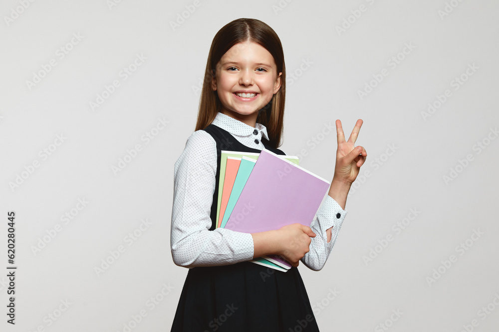 Cheerful child in school uniform carrying textbook and showing peace gesture with big smile, isolated over white background. Back to school concept Cheerful child in school uniform carrying textbook and showing peace gesture with big smile, isolated over white background. Back to school concept