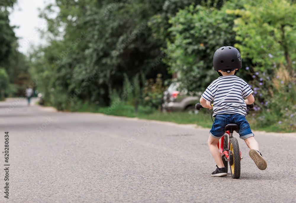 A cheerful little boy rides a running bike in a helmet outdoors. A happy child is engaged in an active sport. Protection. Life insurance and child safety. A cheerful little boy rides a running bike in a helmet outdoors. A happy child is engaged in an active sport. Protection. Life insurance and child safety.