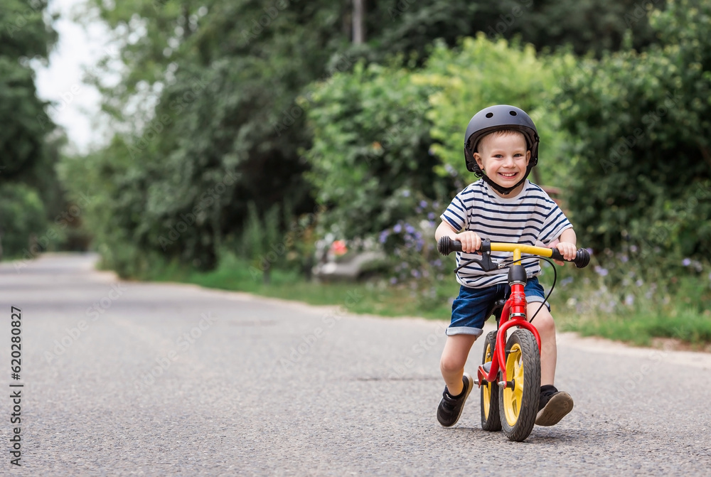 A cheerful little boy rides a running bike in a helmet outdoors. A happy child is engaged in an active sport. Protection. Life insurance and child safety. A cheerful little boy rides a running bike in a helmet outdoors. A happy child is engaged in an active sport. Protection. Life insurance and child safety.