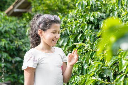 A very happy and smiling little brunette girl holding an Arabica coffee leaf in her hand, while learning and educating herself about this plant