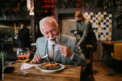Happy businessman sitting in restaurant and having lunch. He is enjoying in delicious food and wine.