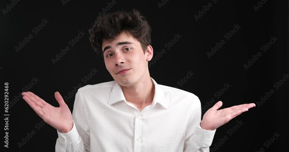 Handsome young Caucasian man as he shrugs his shoulders against a striking black background. With his immaculate appearance and confident demeanor, he exudes an irresistible allure. Handsome young Caucasian man as he shrugs his shoulders against a striking black background. With his immaculate appearance and confident demeanor, he exudes an irresistible allure.