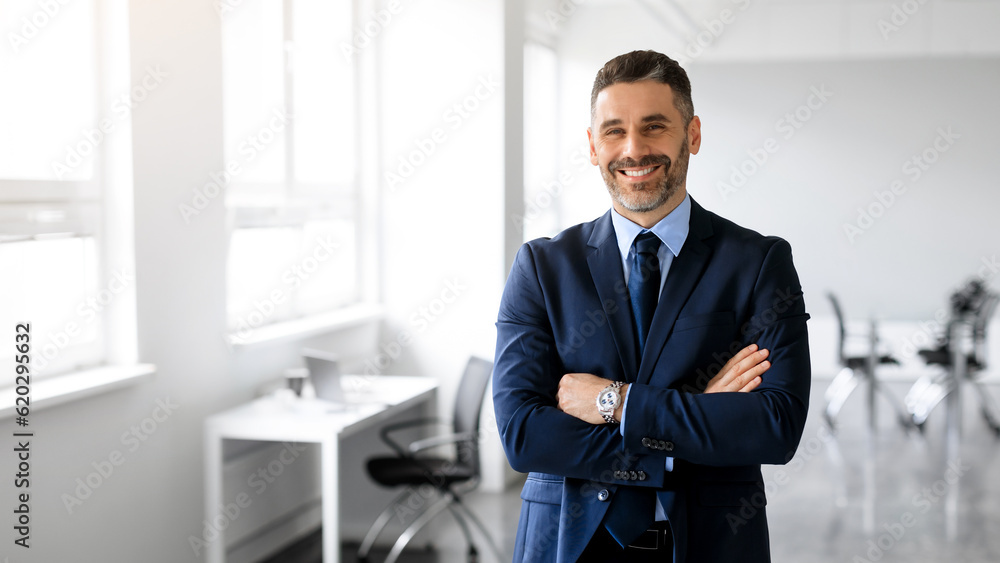 Fototapeta premium Happy middle aged man manager posing with arms crossed in office and smiling at camera, panorama, copy space