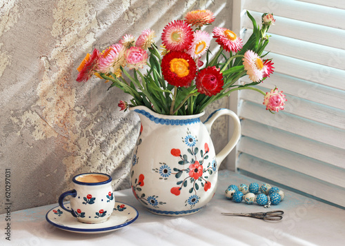 Small ceramic cup with saucers of espresso coffee on the table.  Jug with red and pink flowers. Selective focus. photo