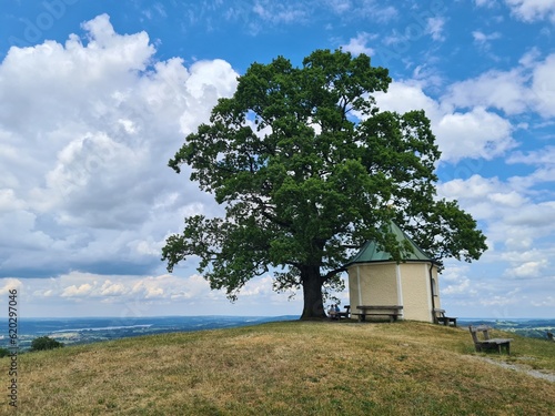 Beautiful view of small rural church Samerberg in summer. Bavaria, Germany, Europe. Small Bavarian chapel on a hill with tree with cloudy sky in background