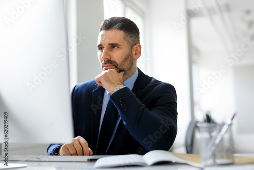 Busy middle aged entrepreneur man working on computer in office, looking at monitor, reading news or corporate emails