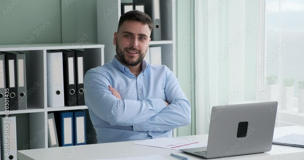 Caucasian businessman with a beard and in business attire is seen working on his laptop at his desk in the office. He turns towards the camera with a big smile, exuding positivity and professionalism. Caucasian businessman with a beard and in business attire is seen working on his laptop at his desk in the office. He turns towards the camera with a big smile, exuding positivity and professionalism.