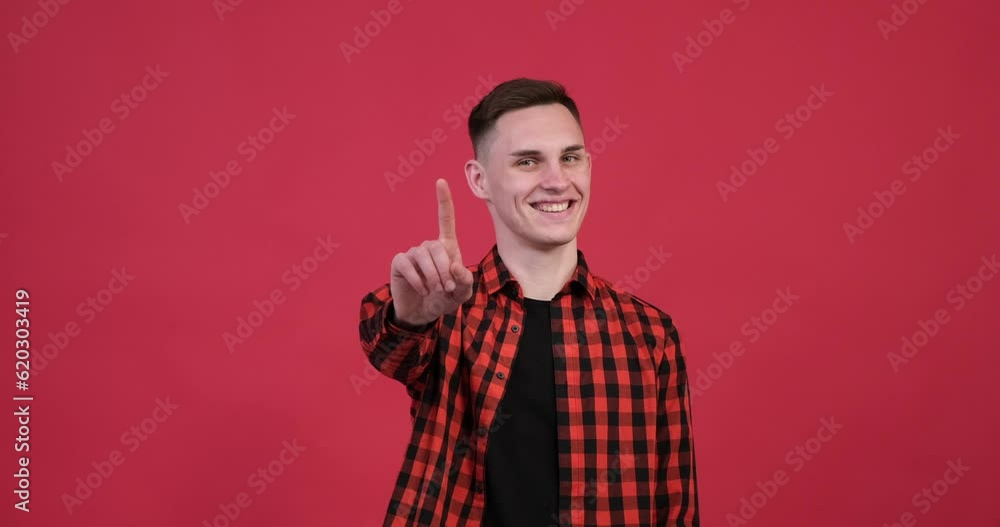 On the vibrant red background, the joyful Caucasian man nods his head and wags his finger in an affirmative gesture. A bright smile illuminates his face as he expresses his agreement or approval. On the vibrant red background, the joyful Caucasian man nods his head and wags his finger in an affirmative gesture. A bright smile illuminates his face as he expresses his agreement or approval.