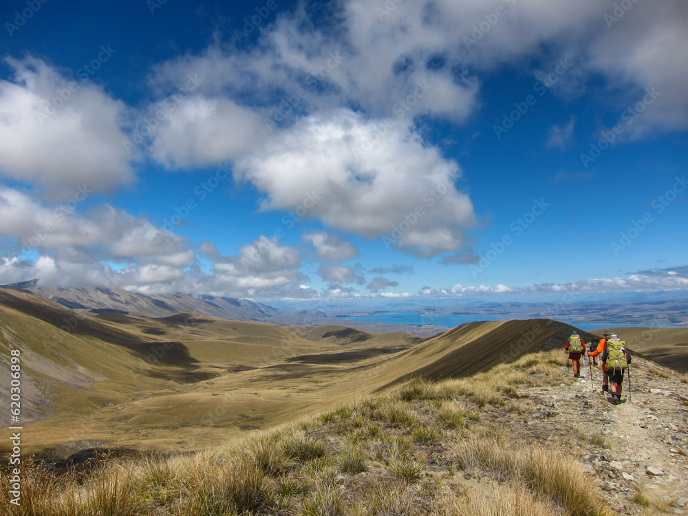 Hikers on a ridgeline in New Zealand along the Te Araroa long distance trail with Lake Tekapo at the horizon