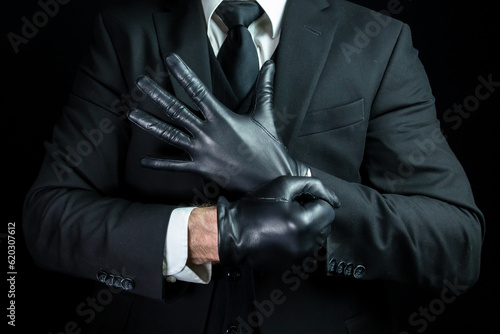 Portrait of Strong Man in Dark Suit Pulling on Gloves. Mobster Putting on Black Leather Gloves.