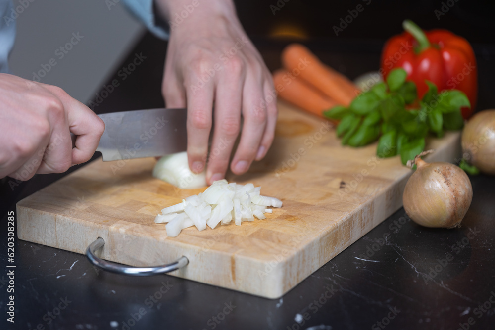 Man in blue shirt cutting and dicing onion og wooden cutting board, with other vegetables in the background. Man in blue shirt cutting and dicing onion og wooden cutting board, with other vegetables in the background.