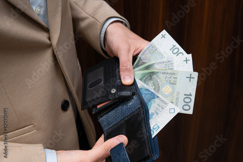 Close-up of Polish money held by a businessman. A man wearing a beige jacket is counting Polish zlotys