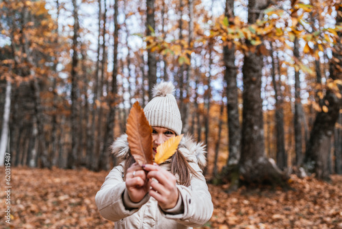 Young woman with wool cap showing a couple of leaves on camera while enjoying an autumn day in the chestnut forest of El Tiemblo  Avila  Spain.