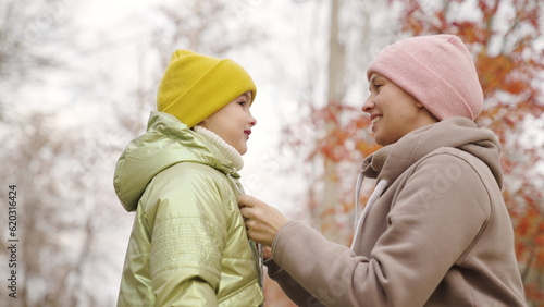 Mom takes care of girl child on street. Family health concept, warm clothes outdoors in autumn, kid outdoors. Happy family, mother straightens her daughters hat and jacket, walk in city autumn park.
