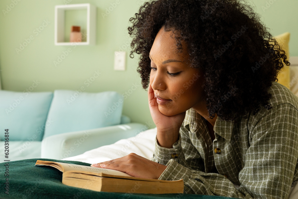 Biracial woman reading book lying on bed in bedroom Biracial woman reading book lying on bed in bedroom