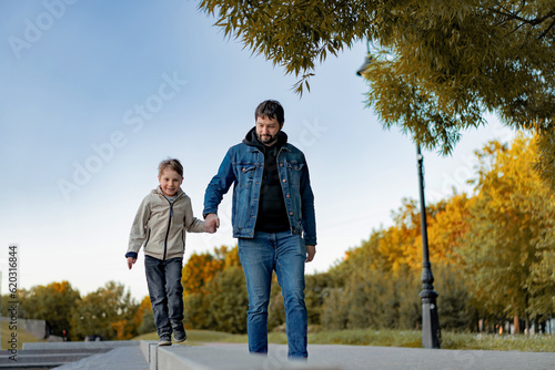 Caucasian bearded man with his little son walking in park holding hands on autumn day