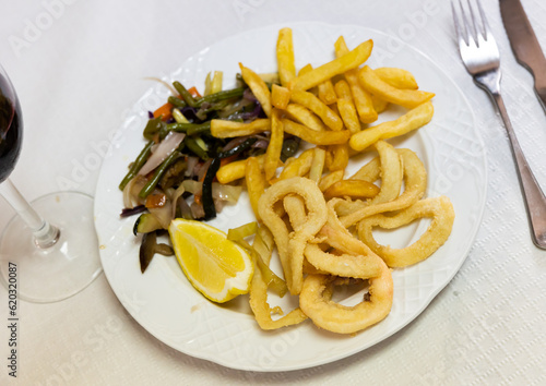 Delicious deep-fried squid rings coated in batter served with garnish of french fries, baked vegetables and slice of lemon Mediterranean cuisine