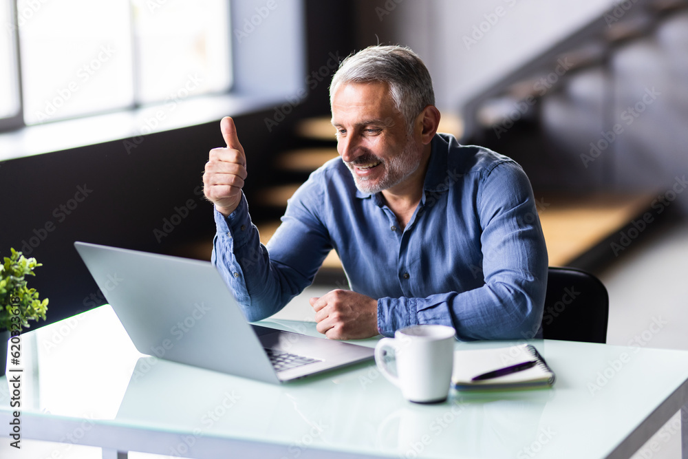 Mature business man waving hand using laptop computer having video conference working online in office. Mature business man waving hand using laptop computer having video conference working online in office.