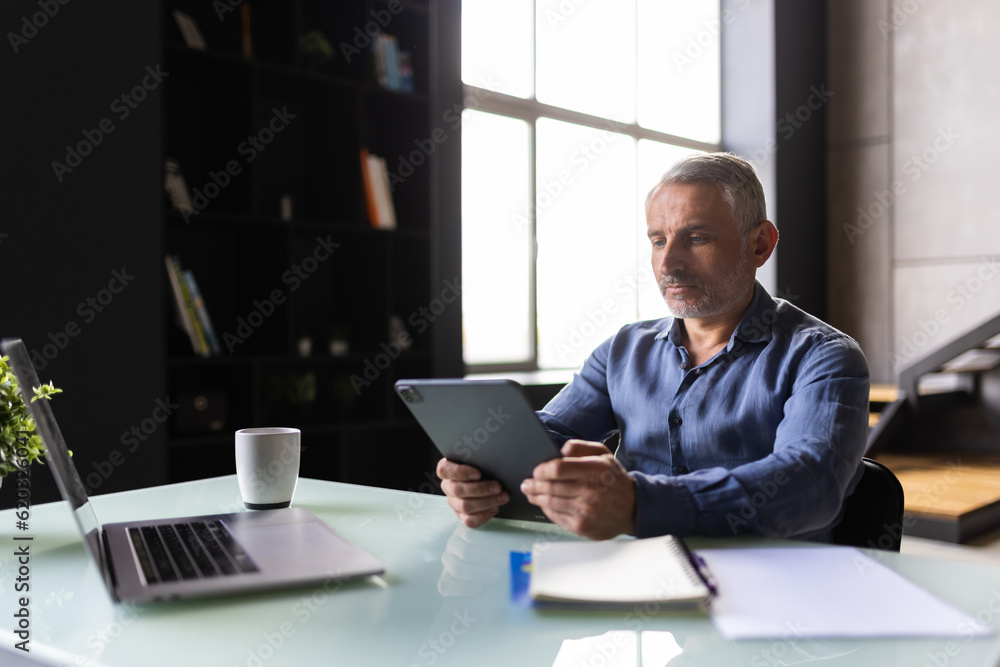Thoughtful smiling mature businessman with tablet pc sitting in office Thoughtful smiling mature businessman with tablet pc sitting in office