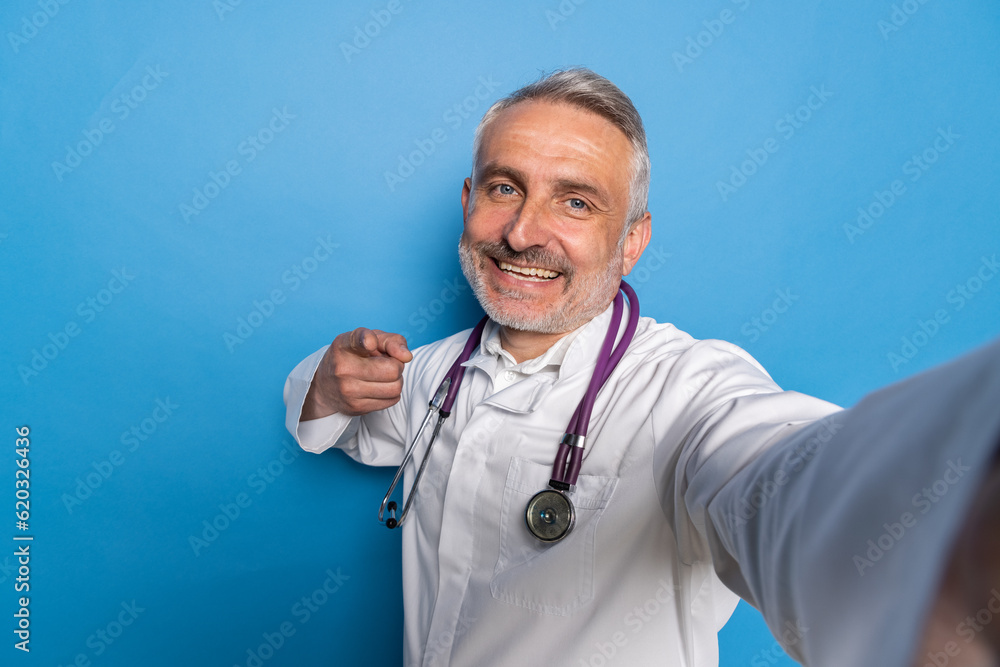 Handsome middle aged doctor using digital tablet to conduct remote appointments on blue background Handsome middle aged doctor using digital tablet to conduct remote appointments on blue background