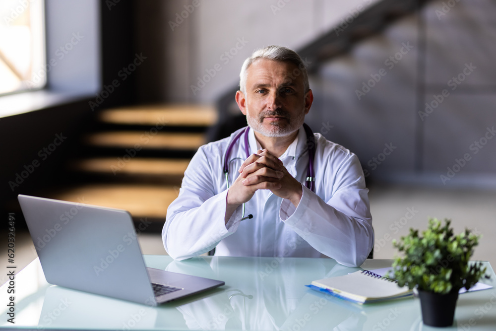 Senior doctor talking with patient using laptop online video webinar consultation while sitting in clinic office. Senior doctor talking with patient using laptop online video webinar consultation while sitting in clinic office.