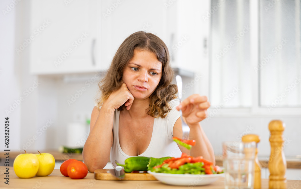 Young woman is not satisfied with prepared salad, refusing to eat vegetables