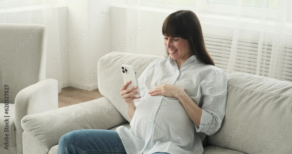 A pregnant woman seated on the couch, she engages with her phone, with a smile on face. Her positive energy and cheerful demeanor shine through as she relishes this moment of relaxation. A pregnant woman seated on the couch, she engages with her phone, with a smile on face. Her positive energy and cheerful demeanor shine through as she relishes this moment of relaxation.