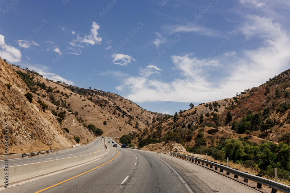 A beautiful highway among mountains with cars and trucks on sunny days. A landscape with transport. Bakersfield, California, USA - 7-22-2021
