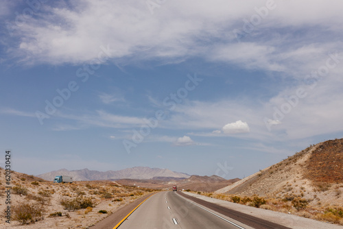 A beautiful asphalt road among hills with dry grass. A scenic landscape with highway, mountains on background and blue sky with fluffy clouds on sunny day. Bakersfield, California, USA - 7-22-2021